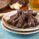 Baltic Fried Bread pieces on two brown plates with beer and garlic cloves in the background.