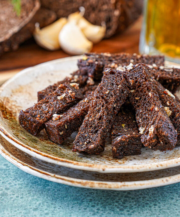 Baltic Fried Bread pieces on two brown plates with beer and garlic cloves in the background.