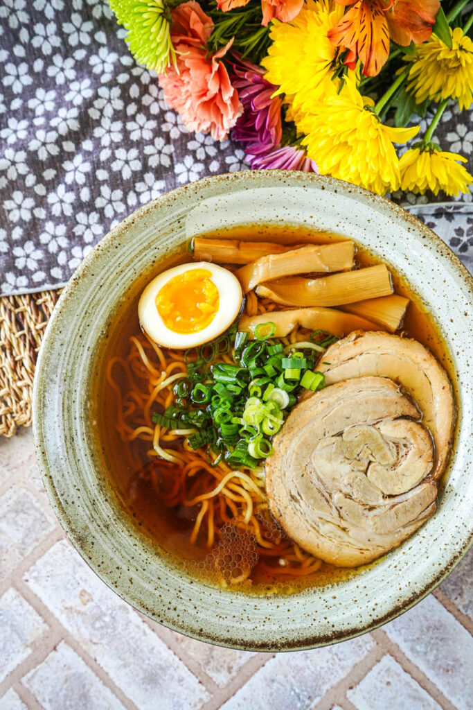 Aerial view of Fastest-Ever Homemade Shoyu Ramen in a bowl next to a bouquet of flowers.