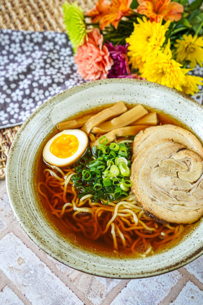 Close up of Fastest-Ever Homemade Shoyu Ramen in a bowl with a bouquet of flowers in the background.
