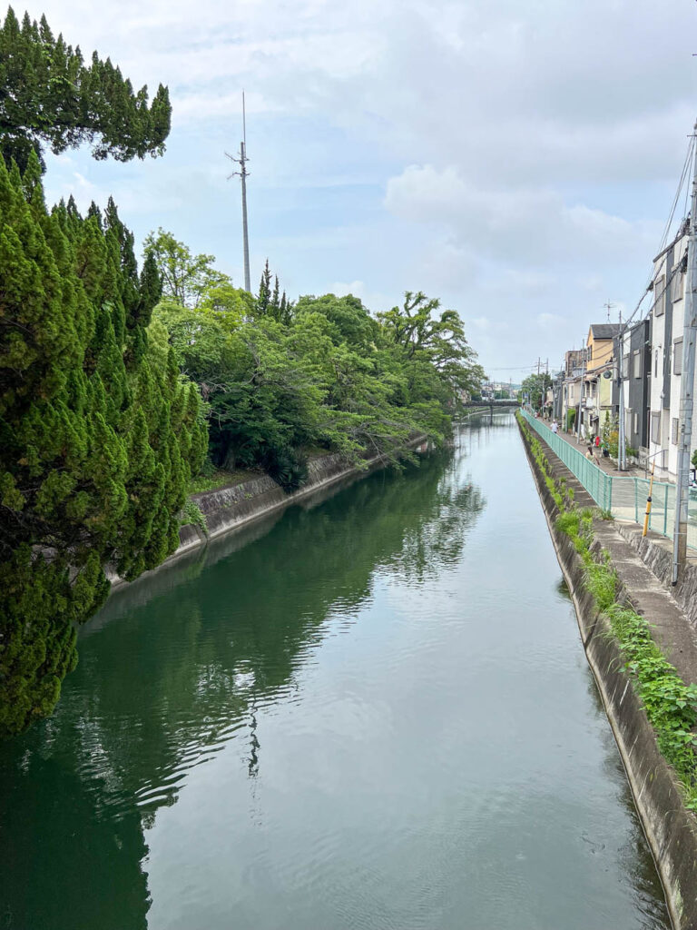 Small canal lined with trees on the left and buildings on the right.