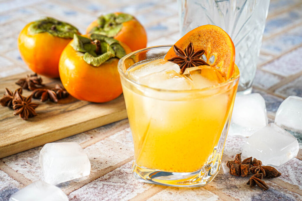 Kaki Sour in a glass with a persimmon slice and a star anise.
