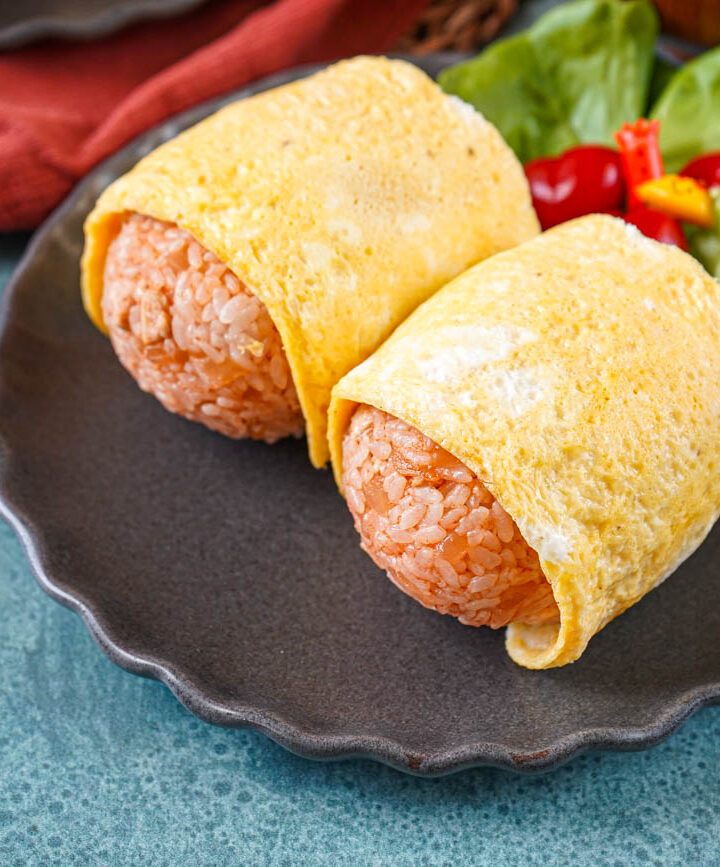 Two Omurice Onigiri on a gray plate with lettuce leaves and cherry tomatoes.