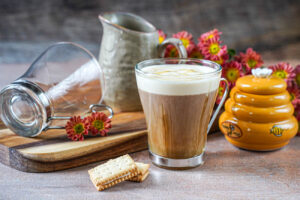 Salted Vanilla Honey Cream Coffee in a glass next to two cookies, a honey jar, and a pitcher.