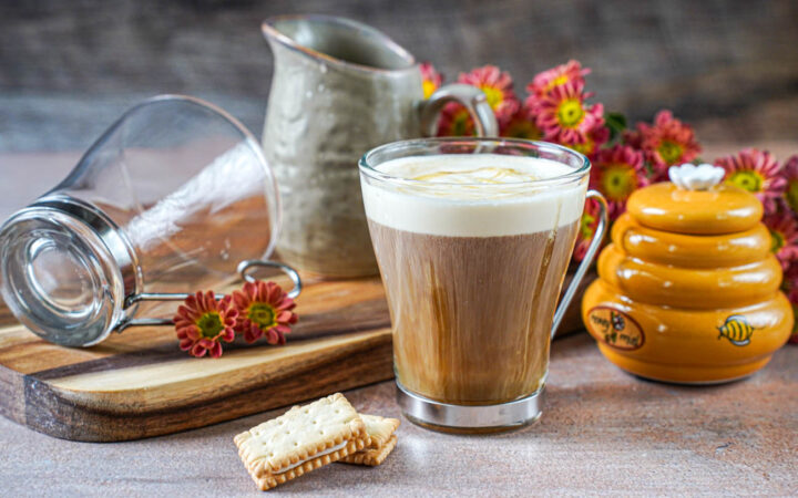 Salted Vanilla Honey Cream Coffee in a glass next to two cookies, a honey jar, and a pitcher.