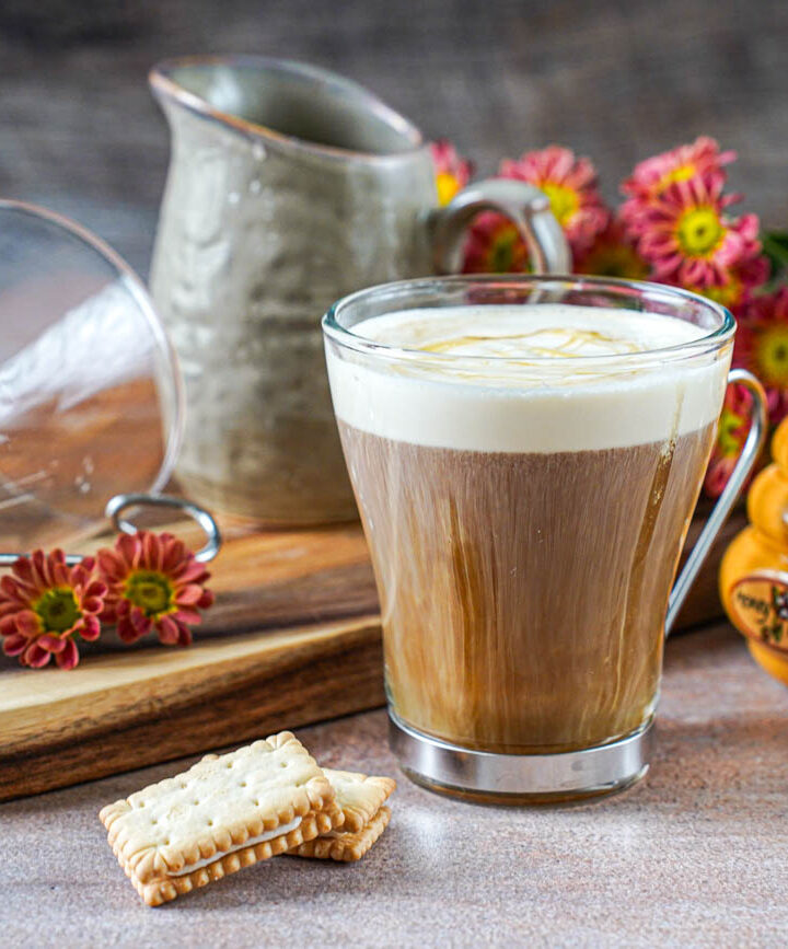 Salted Vanilla Honey Cream Coffee in a glass next to two cookies, a honey jar, and a pitcher.