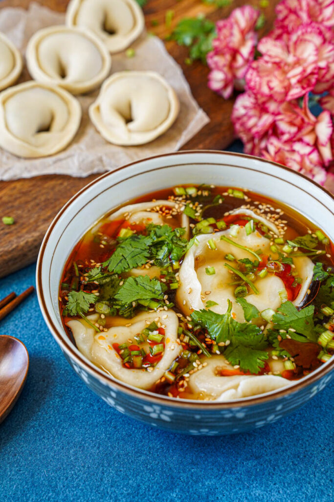 Close up of Shaanxi Dumpling Soup in a bowl with flowers and dumplings in the background.