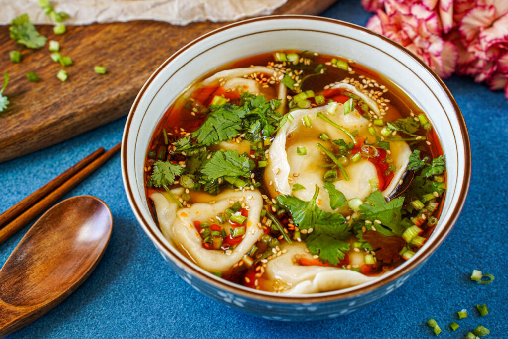 Shaanxi Dumpling Soup in a bowl next to a wooden spoon and chopsticks.