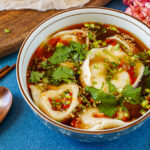 Shaanxi Dumpling Soup in a bowl next to a wooden spoon and chopsticks.