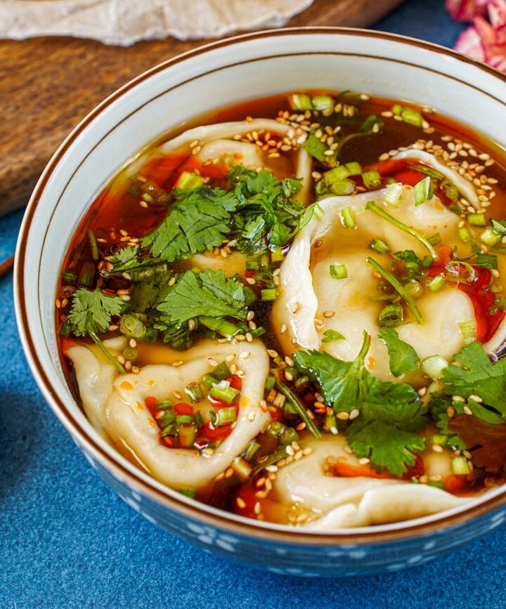 Shaanxi Dumpling Soup in a bowl next to a wooden spoon and chopsticks.