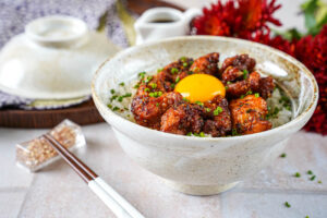 Garlic Butter Crispy Chicken Rice in a bowl next to chopsticks and red flowers.
