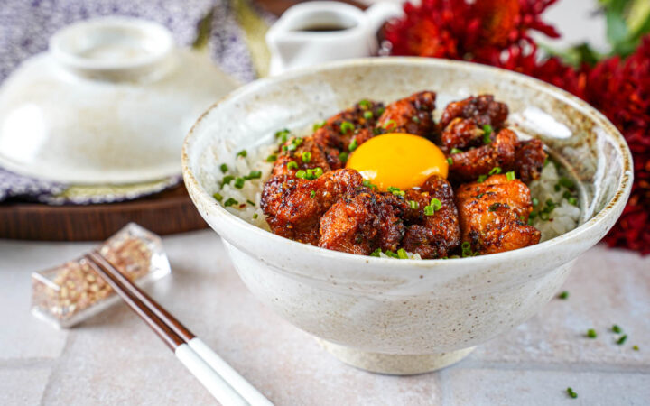 Garlic Butter Crispy Chicken Rice in a bowl next to chopsticks and red flowers.