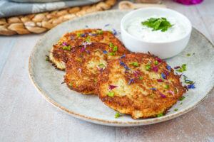 Three Kartoffelpuffer (German Potato Pancakes) on a plate next to Kräuterquark.