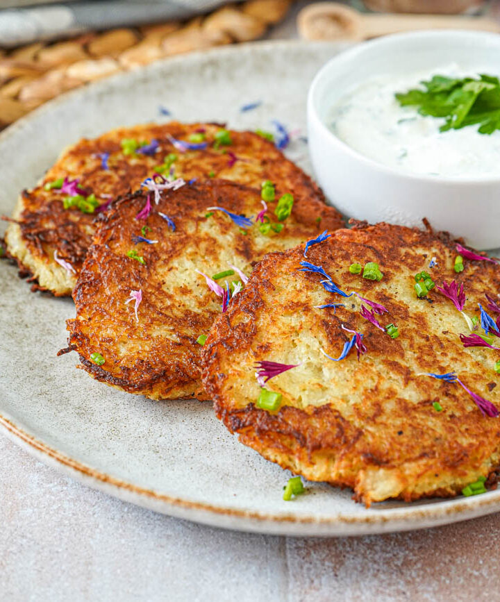 Three Kartoffelpuffer (German Potato Pancakes) on a plate next to Kräuterquark.