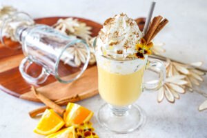 Eierpunsch (German Egg Punch) in a glass mug with a straw, pansy, and two cinnamon sticks.