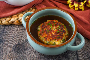 Kaspressknödel (Austrian Cheese Dumpling) in a blue bowl with beef broth.