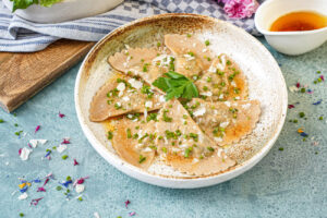 Seven Schlutzkrapfen in a bowl with chopped chives, sliced parmesan, and fresh parsley leaves.