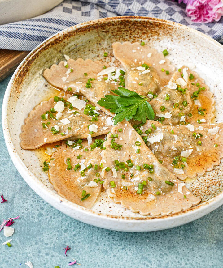 Seven Schlutzkrapfen in a bowl with chopped chives, sliced parmesan, and fresh parsley leaves.