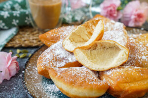 Bur (Cardamom-Spiced Beignets) on a plate with one cut in half to show hollow center.