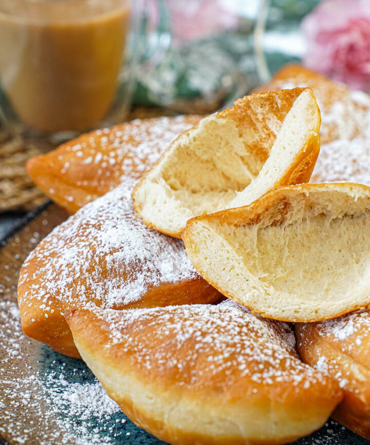 Bur (Cardamom-Spiced Beignets) on a plate with one cut in half to show hollow center.