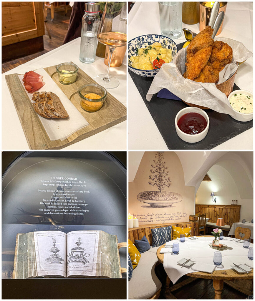 Four photo collage of bread and speck on a board with butter and Liptauer, fried chicken with potato salad, a cookbook on display, and a wooden round table at Gasthof Goldgasse.