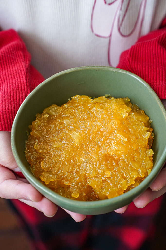 Two hands holding a green bowl of pineapple jam.