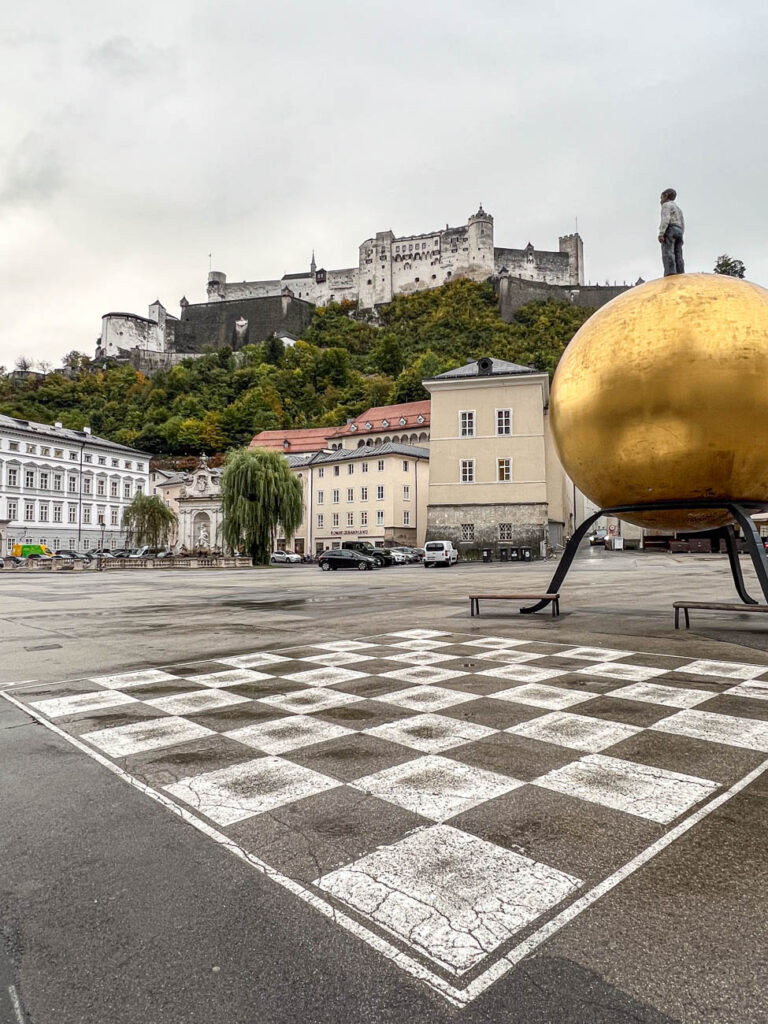 View of Festung Hohensalzburg in the distance with checker board in Salzburg square next to golden ball.