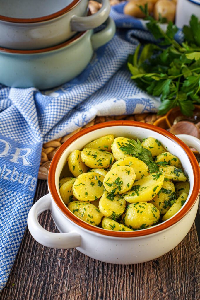 Petersilienerdäpfel (Parsley Potatoes) in a white bowl with three stacked bowls in the background.