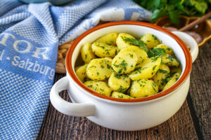 Petersilienerdäpfel (Parsley Potatoes) in a white bowl next to a blue towel.
