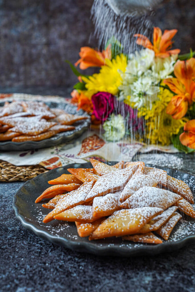 Dusting powdered sugar over a plate of Sakar Para.