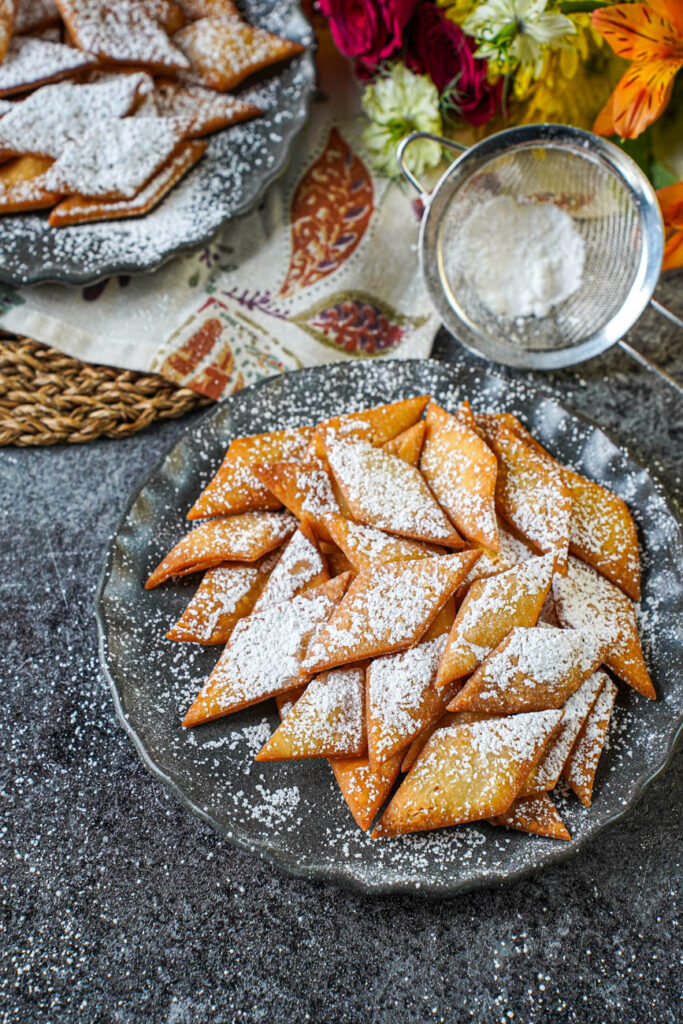 Sakar Para on two plates next to flowers and a sifter with powdered sugar.