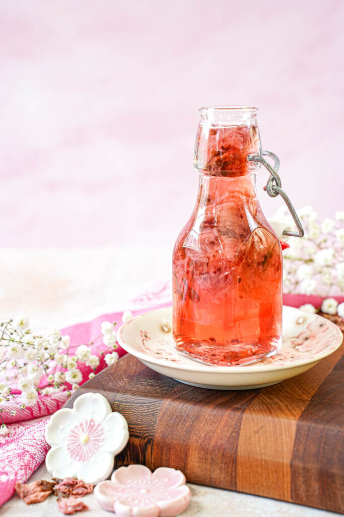 Side view of Cherry Blossom Syrup in a glass jar with white flowers in the background.