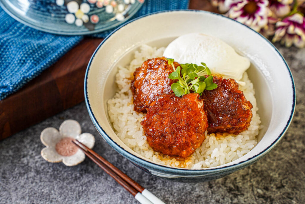 Three Tsukune (Chicken Meatballs) in a bowl with rice, a poached egg, and bok choy sprouts.