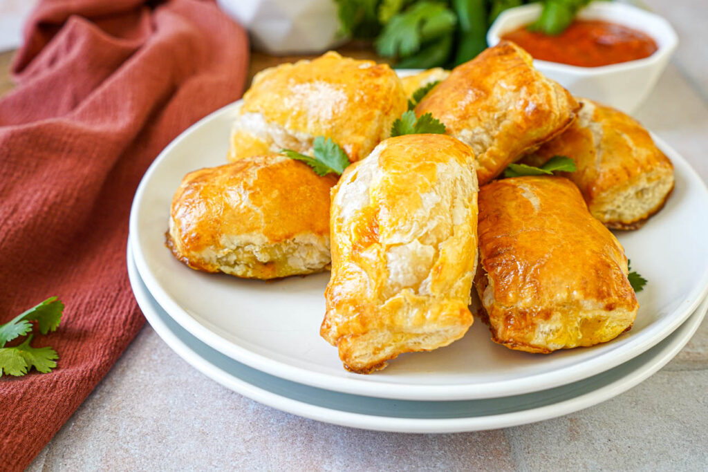 Seven Paneer Masala Puffs on a white plate with cilantro leaves.