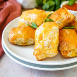 Paneer Masala Puffs on two stacked white plates with fresh cilantro leaves.