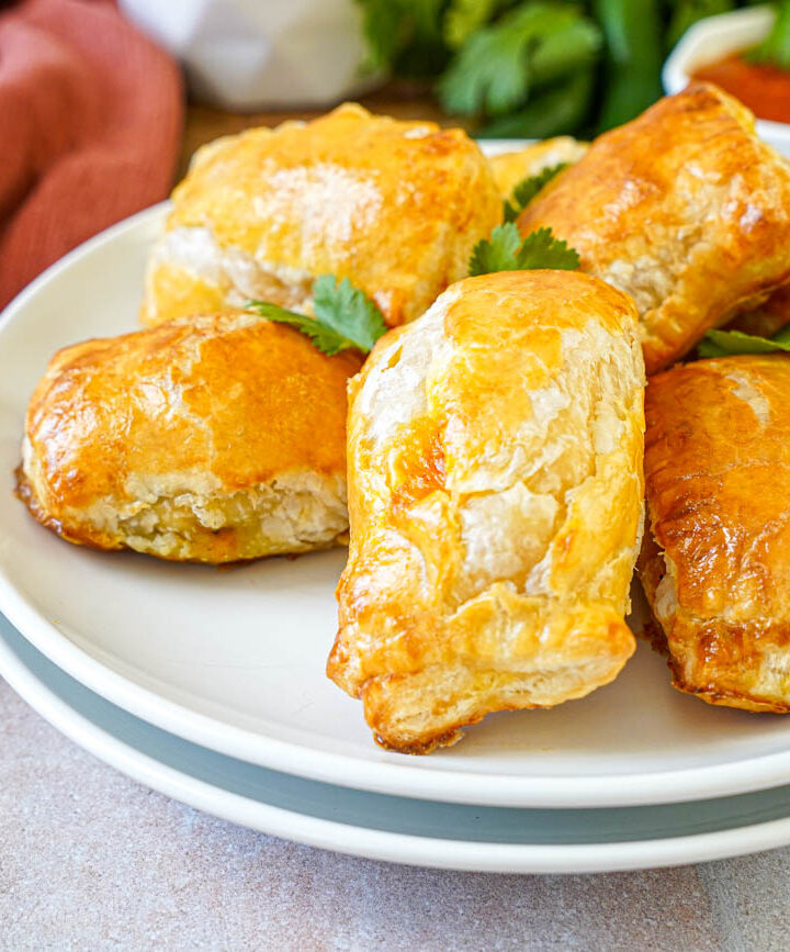 Paneer Masala Puffs on two stacked white plates with fresh cilantro leaves.