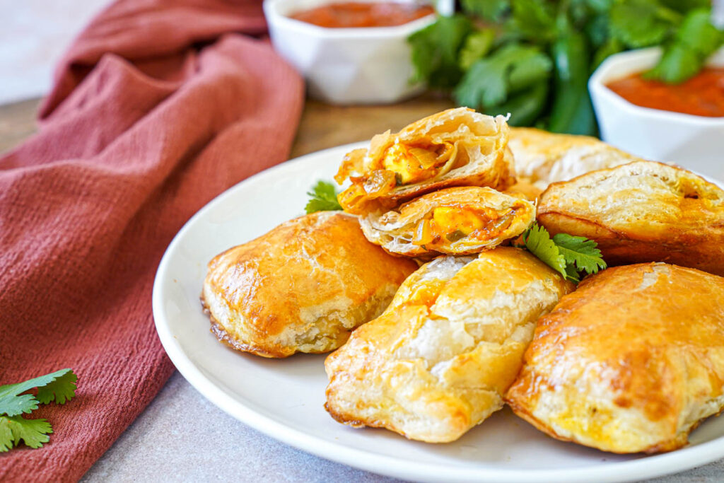 Paneer Masala Puffs on a plate with one cut in half to show paneer filling.