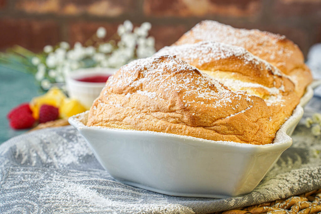 Salzburger Nockerl in a white baking dish with raspberries, lemon wedges, and white flowers in the background.