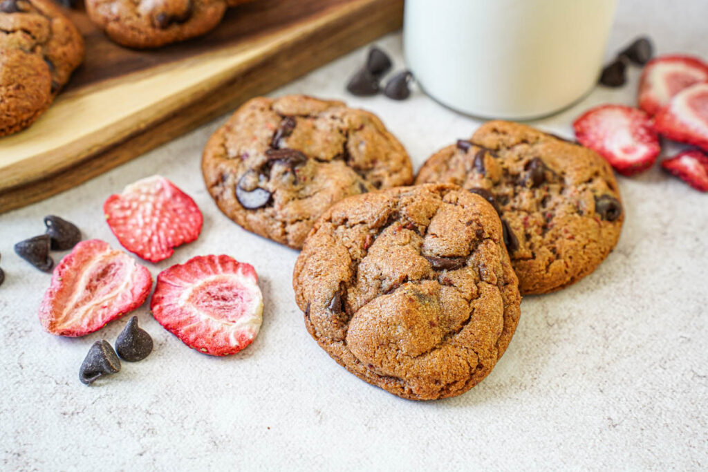 Three Strawberry Chocolate Chip Cookies next to freeze dried strawberry slices and chocolate chips.