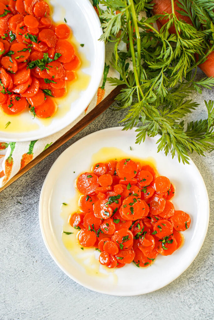 Aerial view of Vichy Carrots (Carottes Vichy) on two plates next to a bunch of carrots and carrot greens.