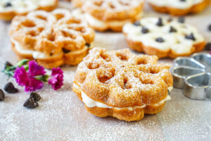 Baci Panteschi (Flower-Shaped Ricotta-Filled Pastries) next to pink flowers and chocolate chips.