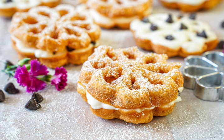 Baci Panteschi (Flower-Shaped Ricotta-Filled Pastries) next to pink flowers and chocolate chips.