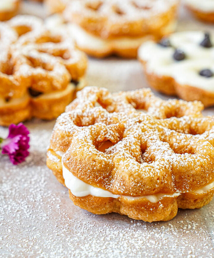 Baci Panteschi (Flower-Shaped Ricotta-Filled Pastries) next to pink flowers and chocolate chips.