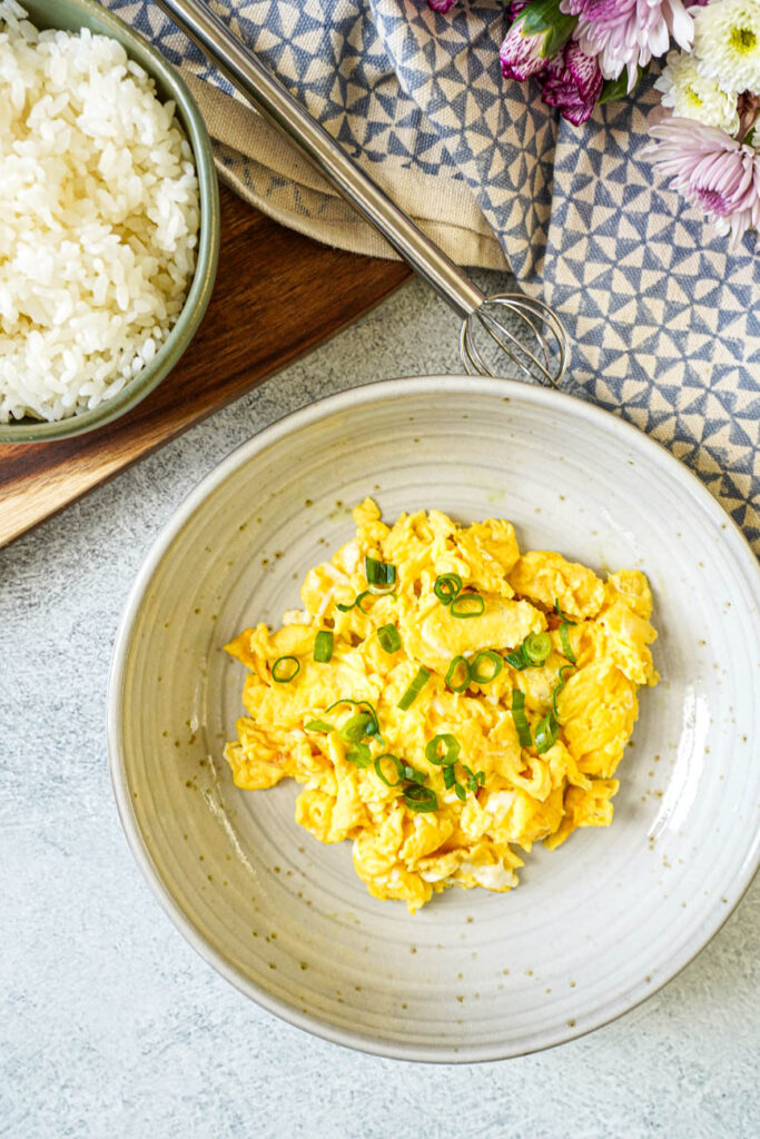 Aerial view of Miso Scrambled Eggs in a bowl next to rice, a miso muddler, and purple flowers.