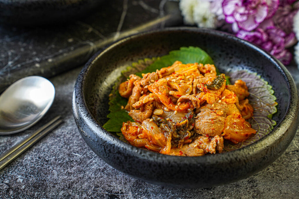 Pork and Kimchi Stir-Fry over perilla leaves in a black bowl.