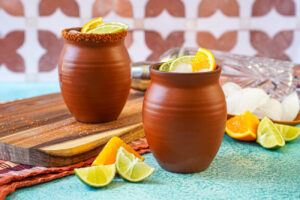 Cantarito in two clay cups next to orange and lime slices.