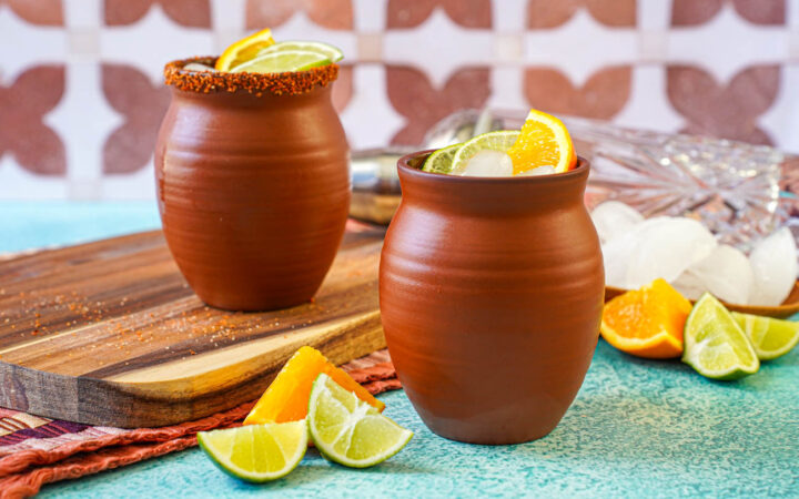Cantarito in two clay cups next to orange and lime slices.