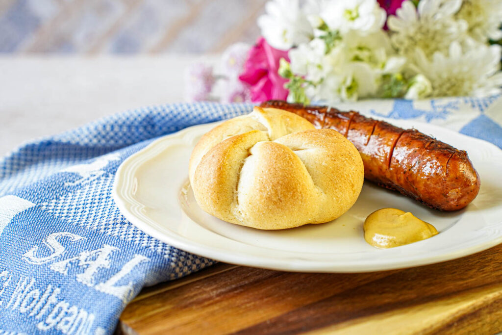 Kaisersemmel on a plate with a sausage and mustard.