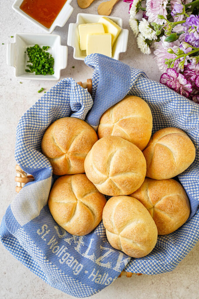Aerial view of Kaisersemmel (Kaiser Rolls) in a basket next to chives, butter, and jam.