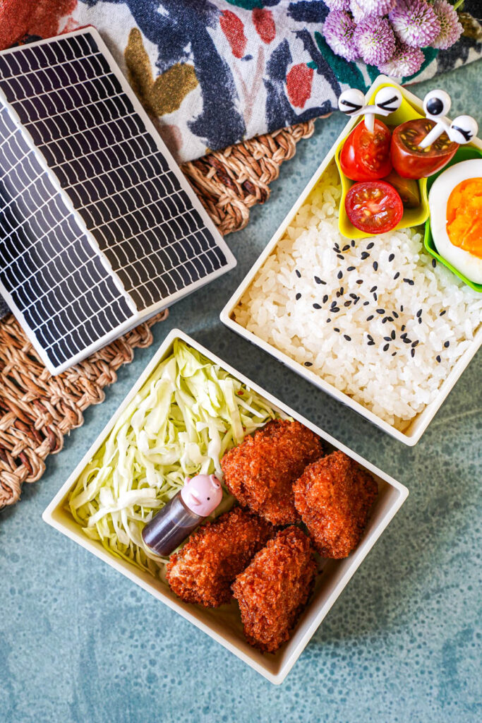 Aerial View of Mini Pork Cutlets in a bento with rice, shredded cabbage, cherry tomatoes, and a hard boiled egg.